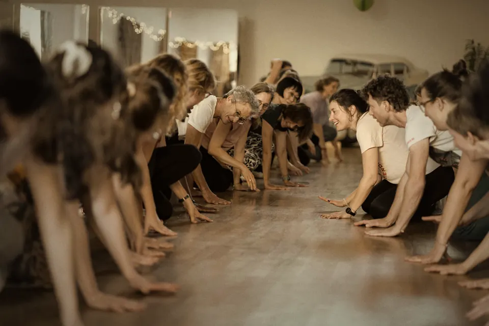 Workshop: zwei Reihen Tanzender beugen sich mit den Händen zum Boden und grinsen sich an