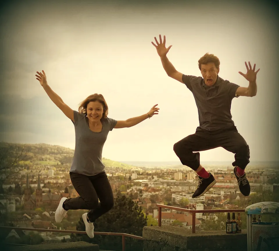 Steve und Maren springen mit hochgerissenen Armen über dem Freiburger Panorama